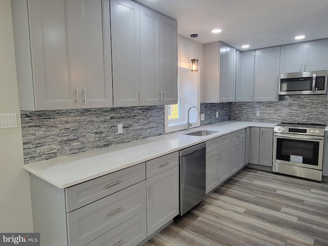 kitchen featuring gray cabinetry, sink, hanging light fixtures, stainless steel appliances, and light wood-type flooring