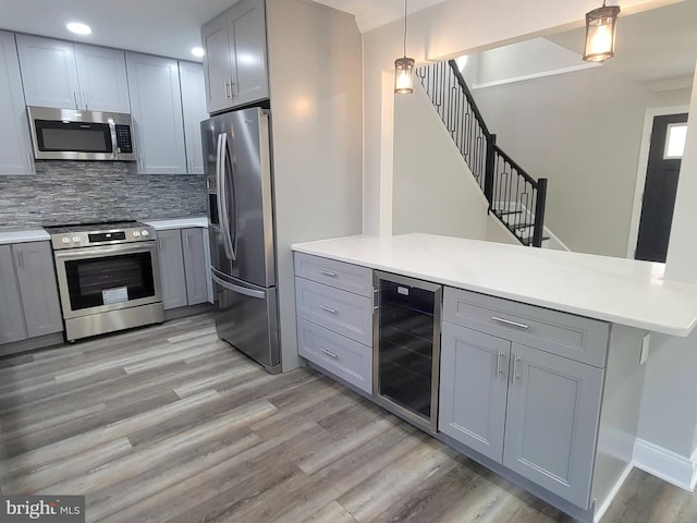 kitchen featuring pendant lighting, beverage cooler, gray cabinetry, and appliances with stainless steel finishes