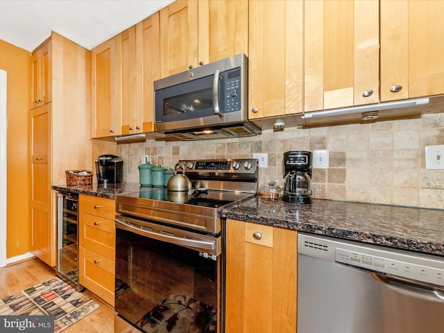 kitchen featuring appliances with stainless steel finishes, backsplash, dark stone counters, light hardwood / wood-style flooring, and wine cooler