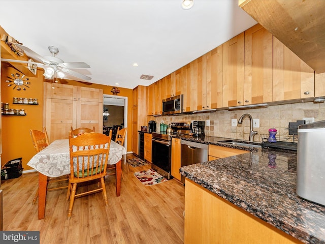 kitchen with light wood-type flooring, tasteful backsplash, stainless steel appliances, sink, and dark stone countertops