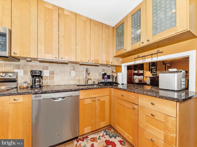 kitchen featuring appliances with stainless steel finishes, backsplash, dark stone counters, and sink