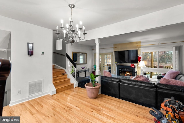 8111 Bird Ln, Greenbelt, MD 20770 - living room featuring ornate columns, stairway, a chandelier, wood finished floors, and a warm lit fireplace