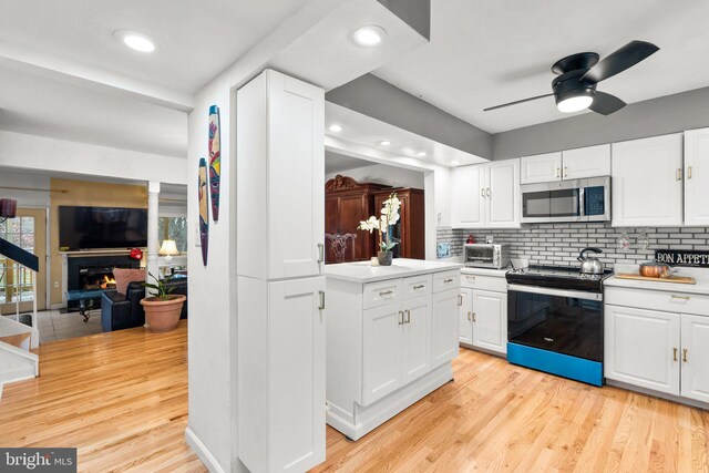 8111 Bird Ln, Greenbelt, MD 20770 - kitchen featuring electric range, stainless steel microwave, a lit fireplace, white cabinetry, and recessed lighting
