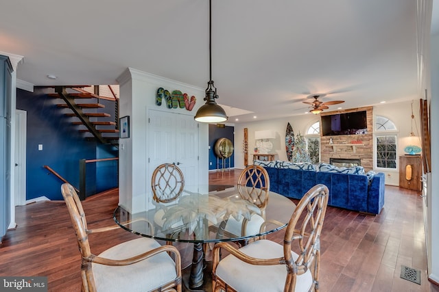 dining area with ceiling fan, a fireplace, crown molding, and dark wood-type flooring