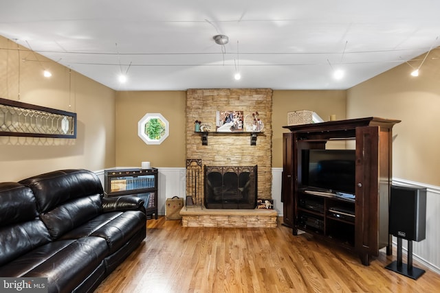 living room featuring a stone fireplace, rail lighting, and wood-type flooring