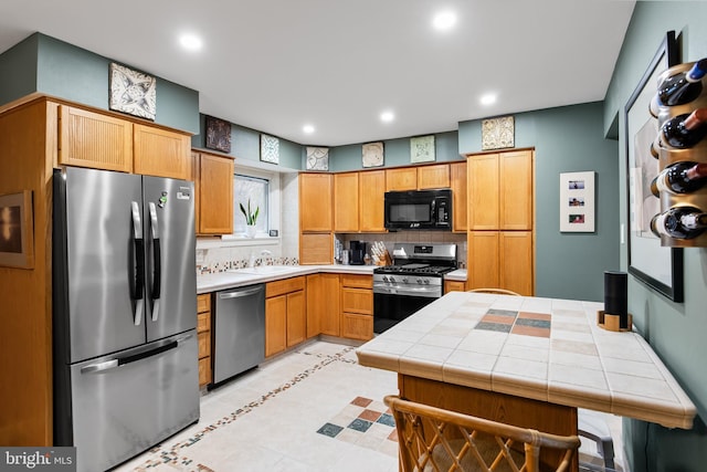 kitchen with tasteful backsplash, stainless steel appliances, sink, tile counters, and light tile patterned flooring