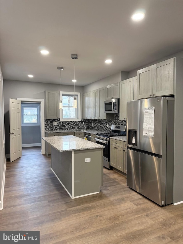 kitchen with light stone countertops, a center island, stainless steel appliances, wood-type flooring, and decorative light fixtures