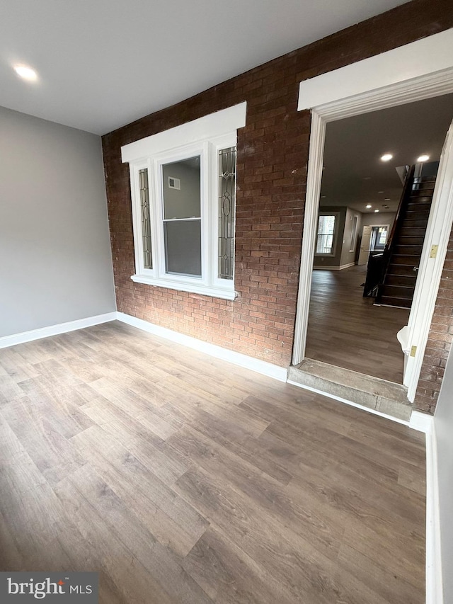 spare room featuring wood-type flooring and brick wall