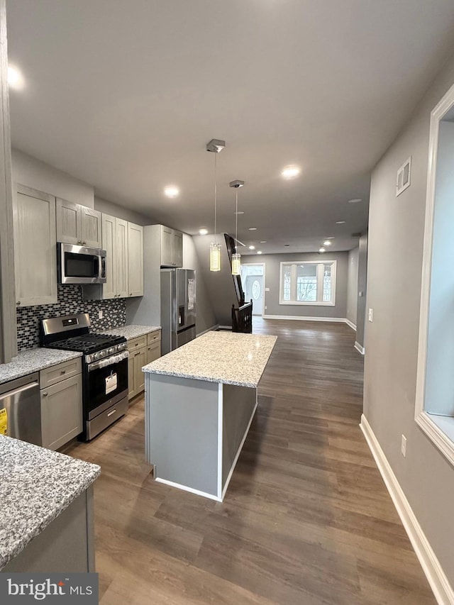 kitchen with light stone countertops, hanging light fixtures, dark hardwood / wood-style floors, and appliances with stainless steel finishes