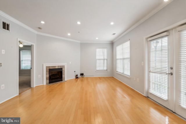 unfurnished living room with a tiled fireplace, crown molding, and light hardwood / wood-style flooring