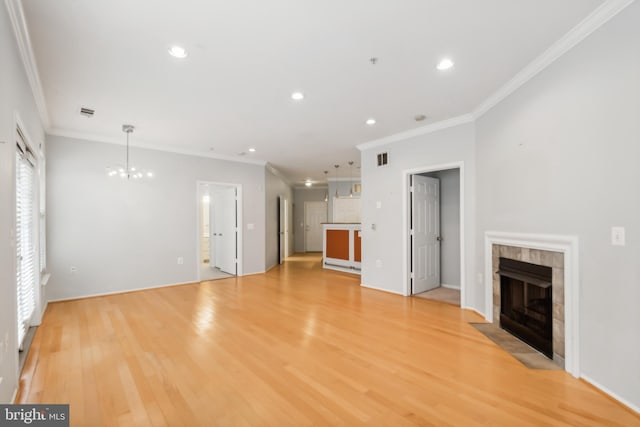 unfurnished living room featuring a fireplace, light hardwood / wood-style floors, crown molding, and an inviting chandelier