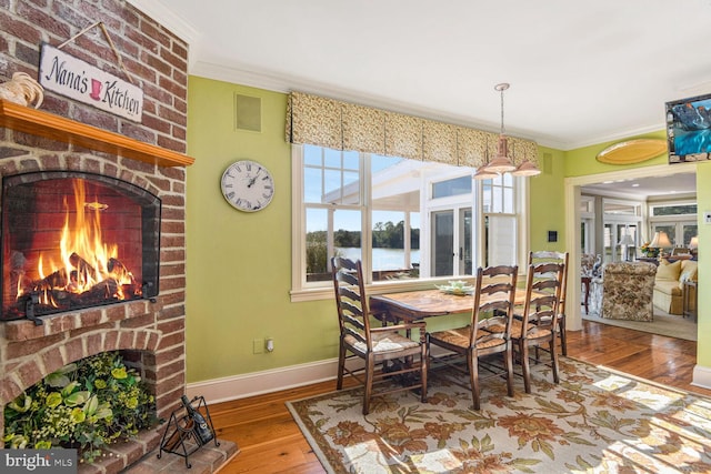 dining space featuring a fireplace, a water view, wood-type flooring, and ornamental molding