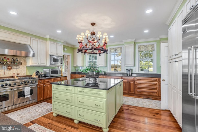 kitchen featuring wall chimney range hood, light hardwood / wood-style flooring, built in appliances, a notable chandelier, and a kitchen island