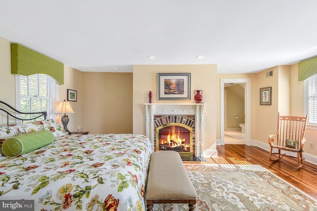 bedroom with hardwood / wood-style floors, a brick fireplace, and ensuite bath