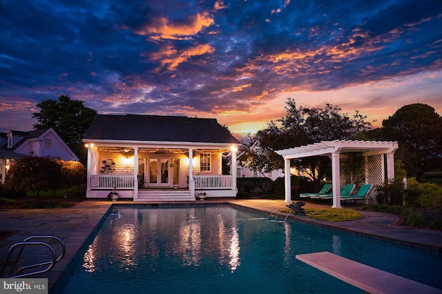 pool at dusk with a diving board, an outbuilding, a pergola, and a patio area