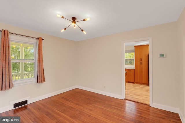 unfurnished room featuring a chandelier, a healthy amount of sunlight, and light hardwood / wood-style flooring