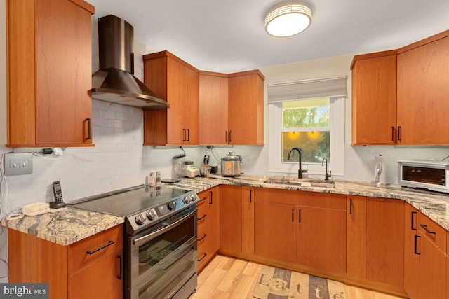 kitchen with stainless steel electric range, sink, wall chimney exhaust hood, light hardwood / wood-style floors, and light stone counters