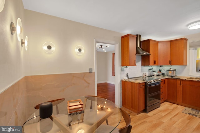 kitchen with light stone countertops, light wood-type flooring, wall chimney range hood, and black range with electric cooktop