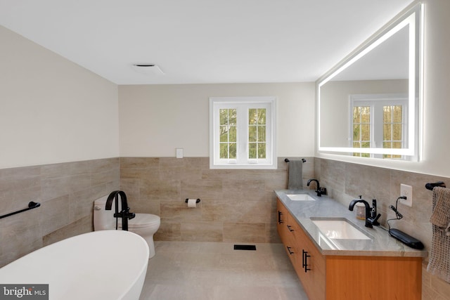 bathroom featuring vanity, a bathing tub, tile patterned flooring, toilet, and tile walls