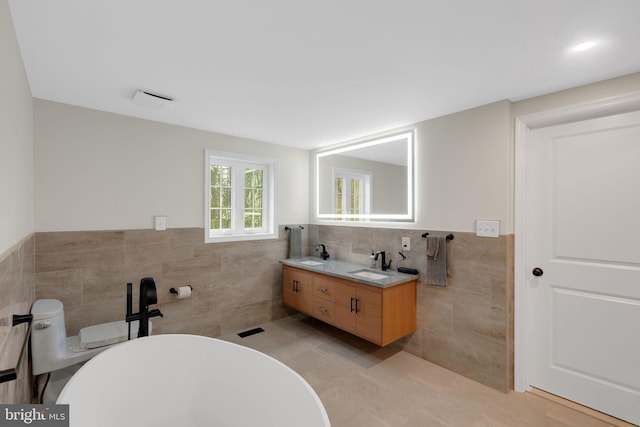 bathroom featuring a tub to relax in, vanity, and tile walls