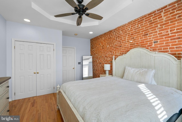 bedroom featuring light hardwood / wood-style floors, brick wall, ceiling fan, and a tray ceiling