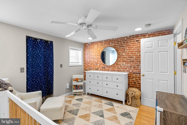 bedroom with brick wall, a nursery area, light wood-type flooring, and ceiling fan