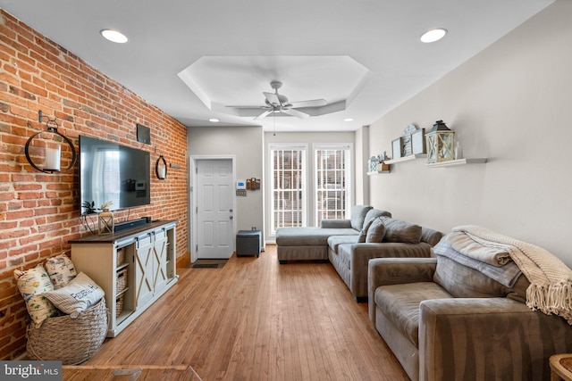 living room featuring light hardwood / wood-style floors, a raised ceiling, ceiling fan, and brick wall