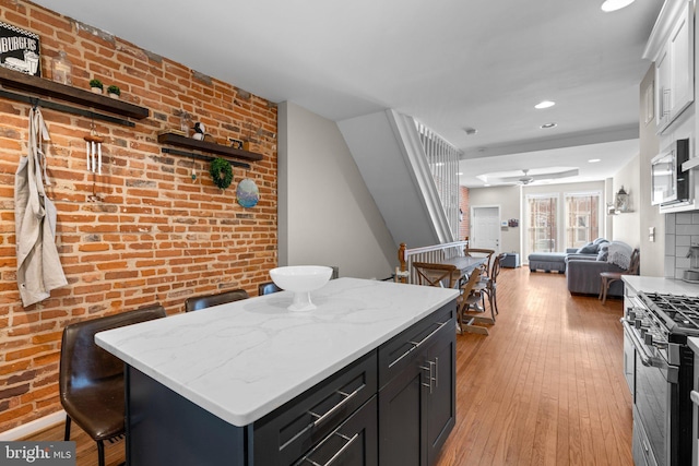 kitchen featuring a breakfast bar area, light hardwood / wood-style flooring, stainless steel range with gas stovetop, a kitchen island, and brick wall