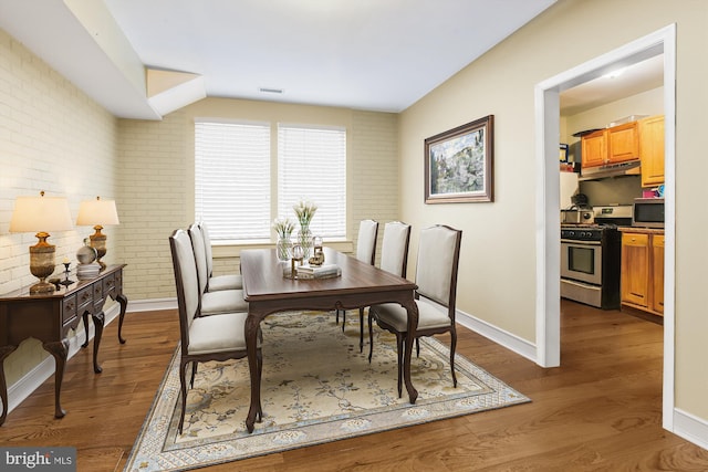 dining space with brick wall, wood-type flooring, and lofted ceiling