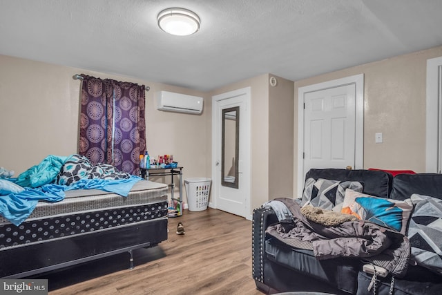 bedroom featuring an AC wall unit, wood-type flooring, and a textured ceiling