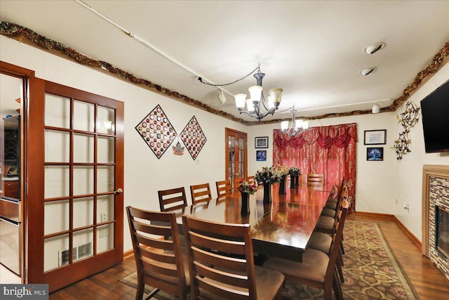 dining space featuring a tiled fireplace, a chandelier, and dark wood-type flooring