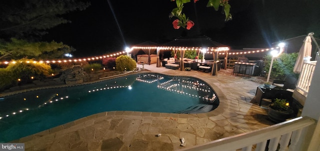 pool at night with an outdoor living space and a patio