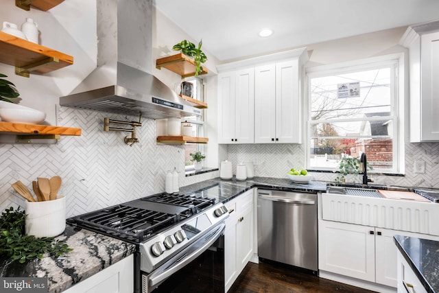 kitchen featuring wall chimney exhaust hood, white cabinetry, appliances with stainless steel finishes, and tasteful backsplash