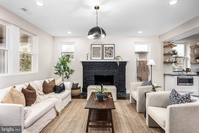 living room with a brick fireplace, plenty of natural light, and light hardwood / wood-style flooring