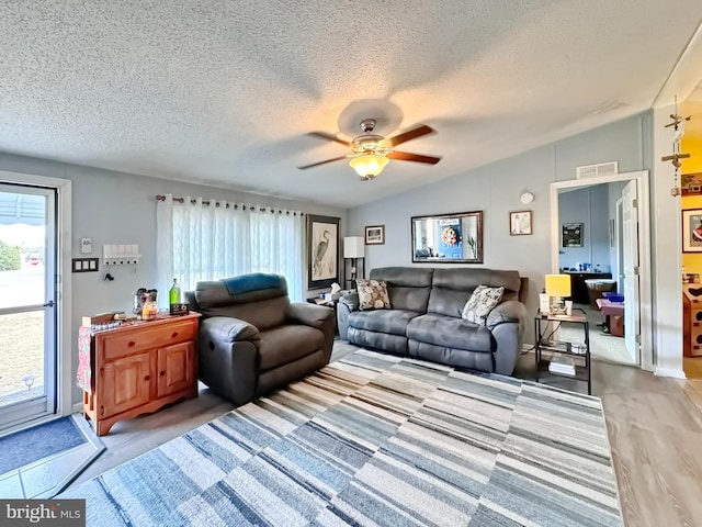 living room with ceiling fan, wood-type flooring, a textured ceiling, and vaulted ceiling