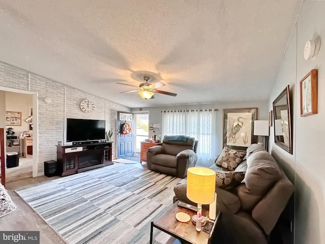 living room featuring ceiling fan, wood-type flooring, a textured ceiling, and vaulted ceiling