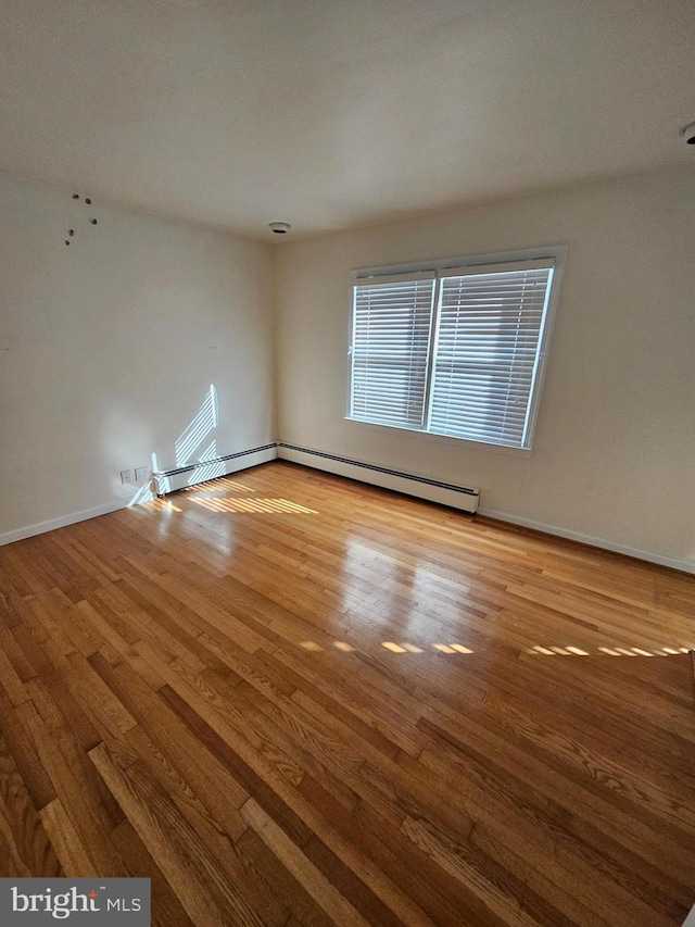 unfurnished room featuring wood-type flooring and a baseboard heating unit