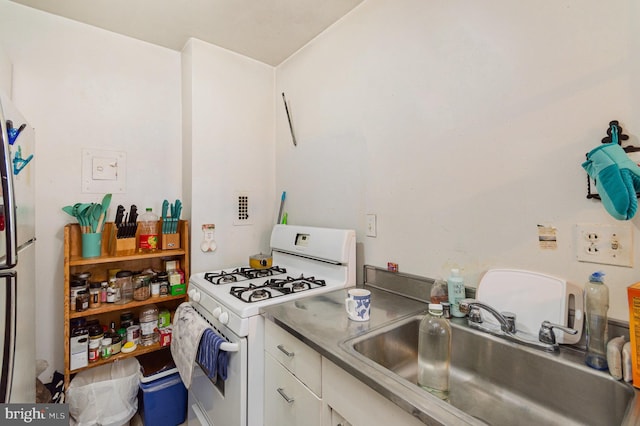 kitchen with stainless steel refrigerator, white range with gas cooktop, white cabinetry, and sink