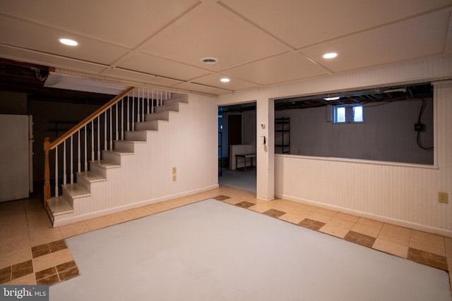 basement featuring a paneled ceiling, white fridge, and wooden walls