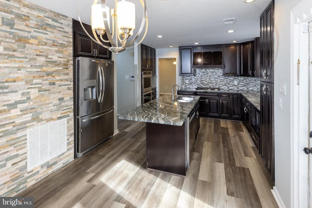 kitchen featuring stone counters, appliances with stainless steel finishes, pendant lighting, tasteful backsplash, and an island with sink