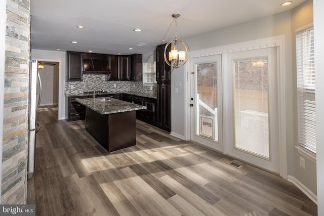 kitchen with custom exhaust hood, decorative light fixtures, dark brown cabinets, a kitchen island, and decorative backsplash