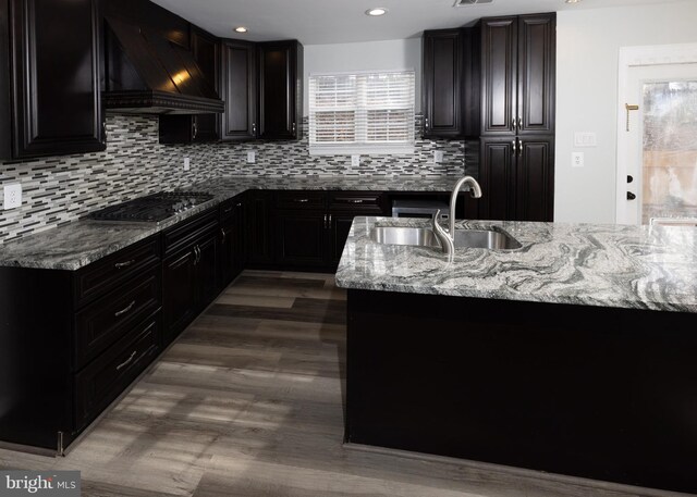 kitchen featuring sink, light stone countertops, custom range hood, stainless steel gas cooktop, and decorative backsplash