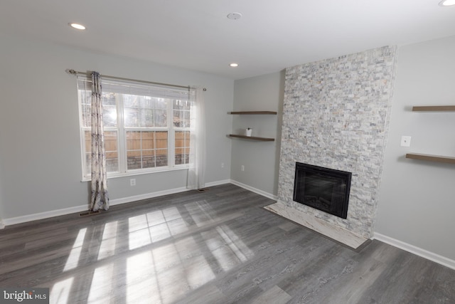 unfurnished living room with dark wood-type flooring and a stone fireplace