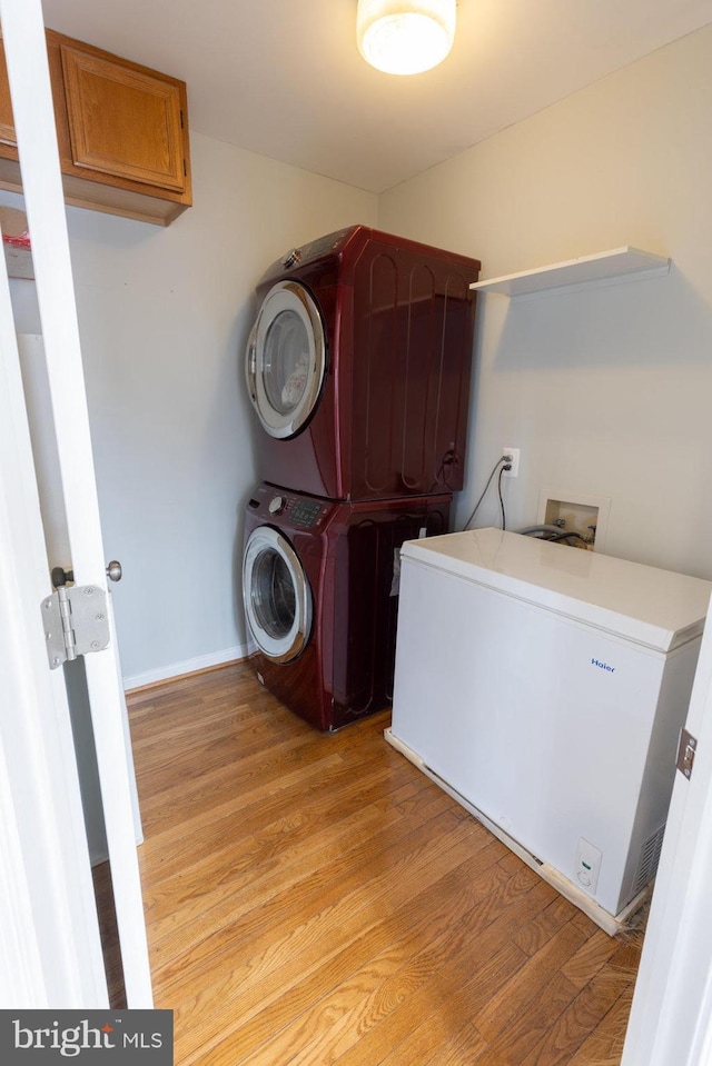 clothes washing area with cabinets, stacked washer / drying machine, and light wood-type flooring