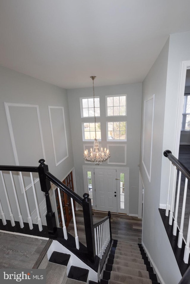 stairway with plenty of natural light, a towering ceiling, hardwood / wood-style floors, and an inviting chandelier