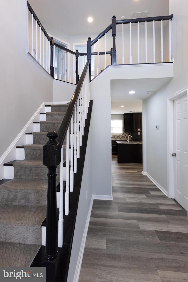 stairway featuring sink, a towering ceiling, and hardwood / wood-style floors