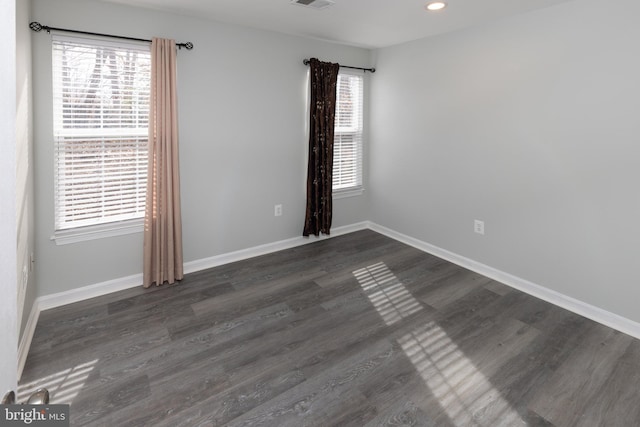 empty room with a wealth of natural light and dark hardwood / wood-style flooring