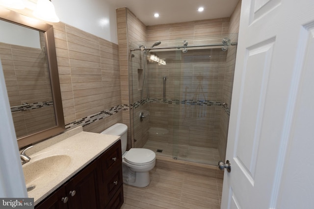 bathroom featuring vanity, toilet, an enclosed shower, and tile walls