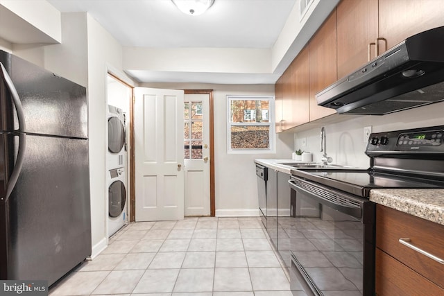 kitchen featuring black appliances, stacked washer / drying machine, light tile patterned floors, and sink