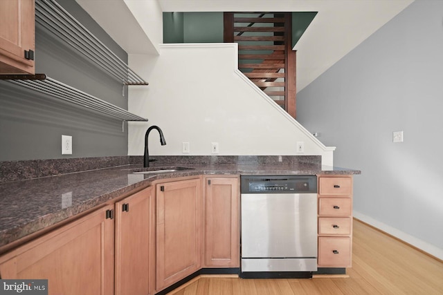 kitchen with light brown cabinets, sink, stainless steel dishwasher, dark stone countertops, and light wood-type flooring